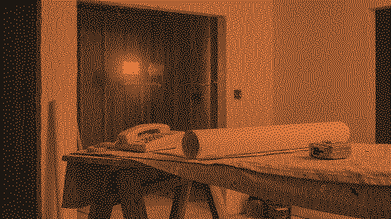 A corded desk phone resting on a sawhorse table beside a blank roll of plans and a tape measure in a half-finished kitchen remodel, a warm orange work light glowing in the framed doorway behind.